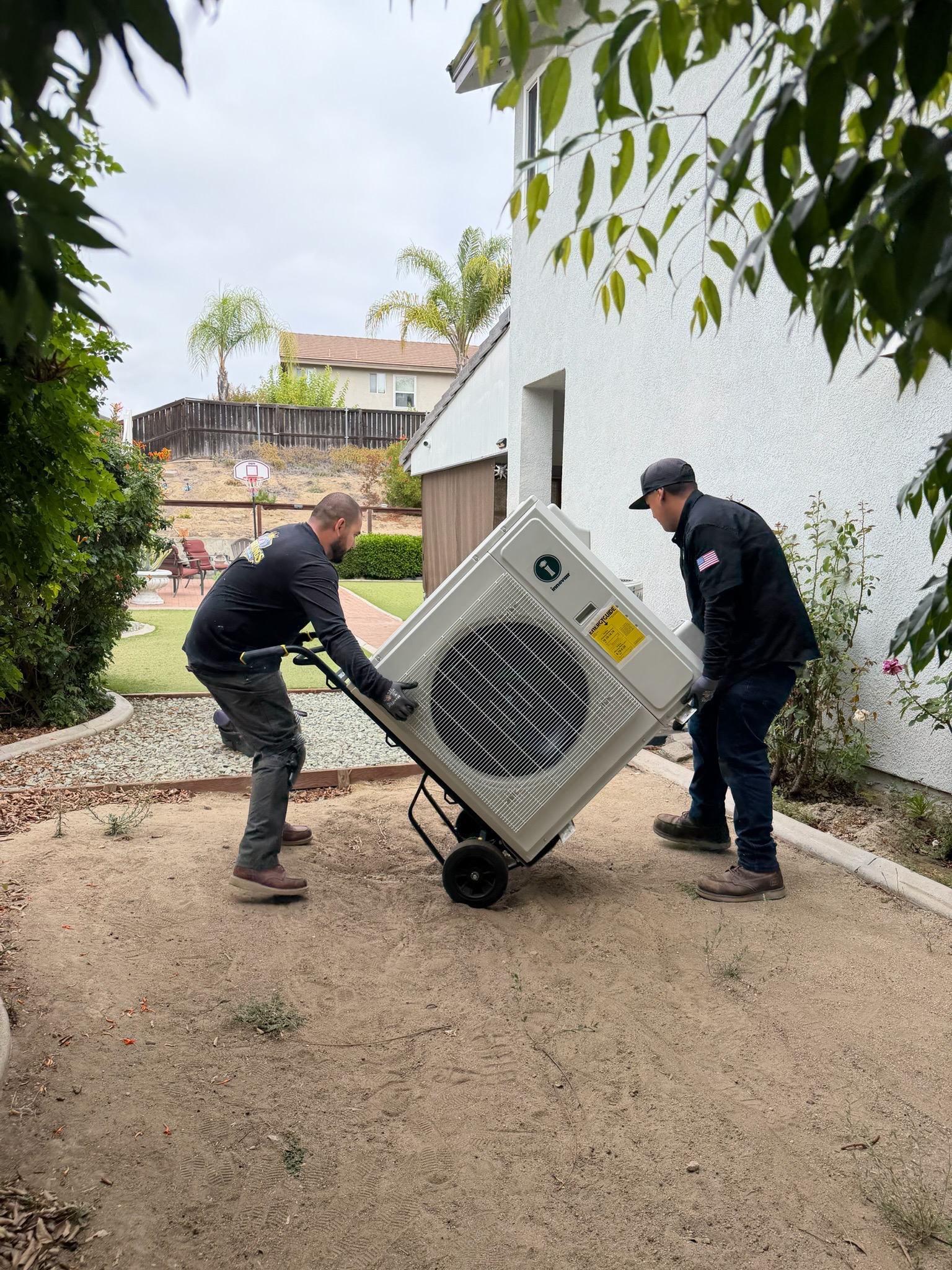 David and Caesar carrying a new unit into a side yard