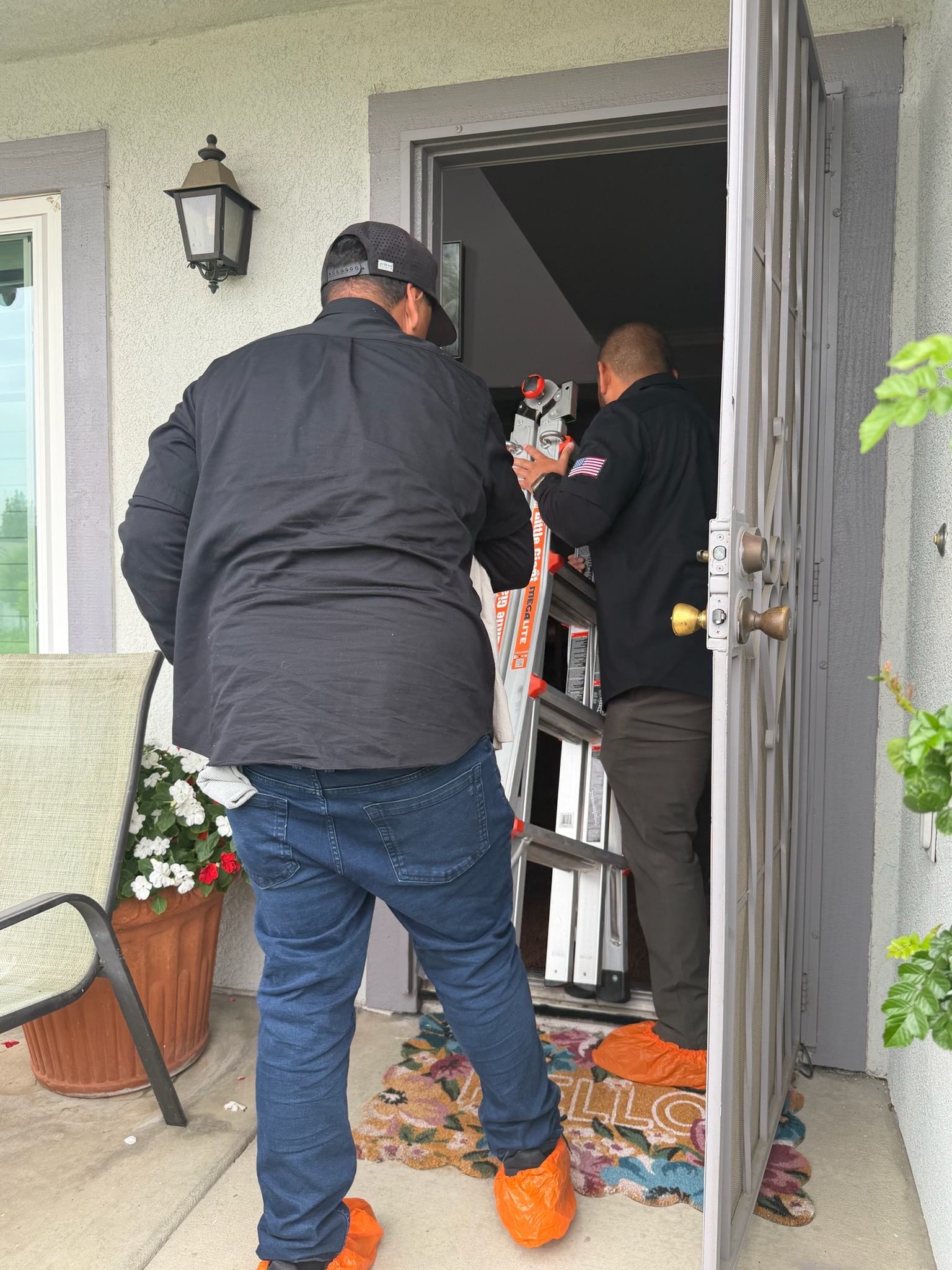 Technicians in shoe covers carrying equipment through a front door